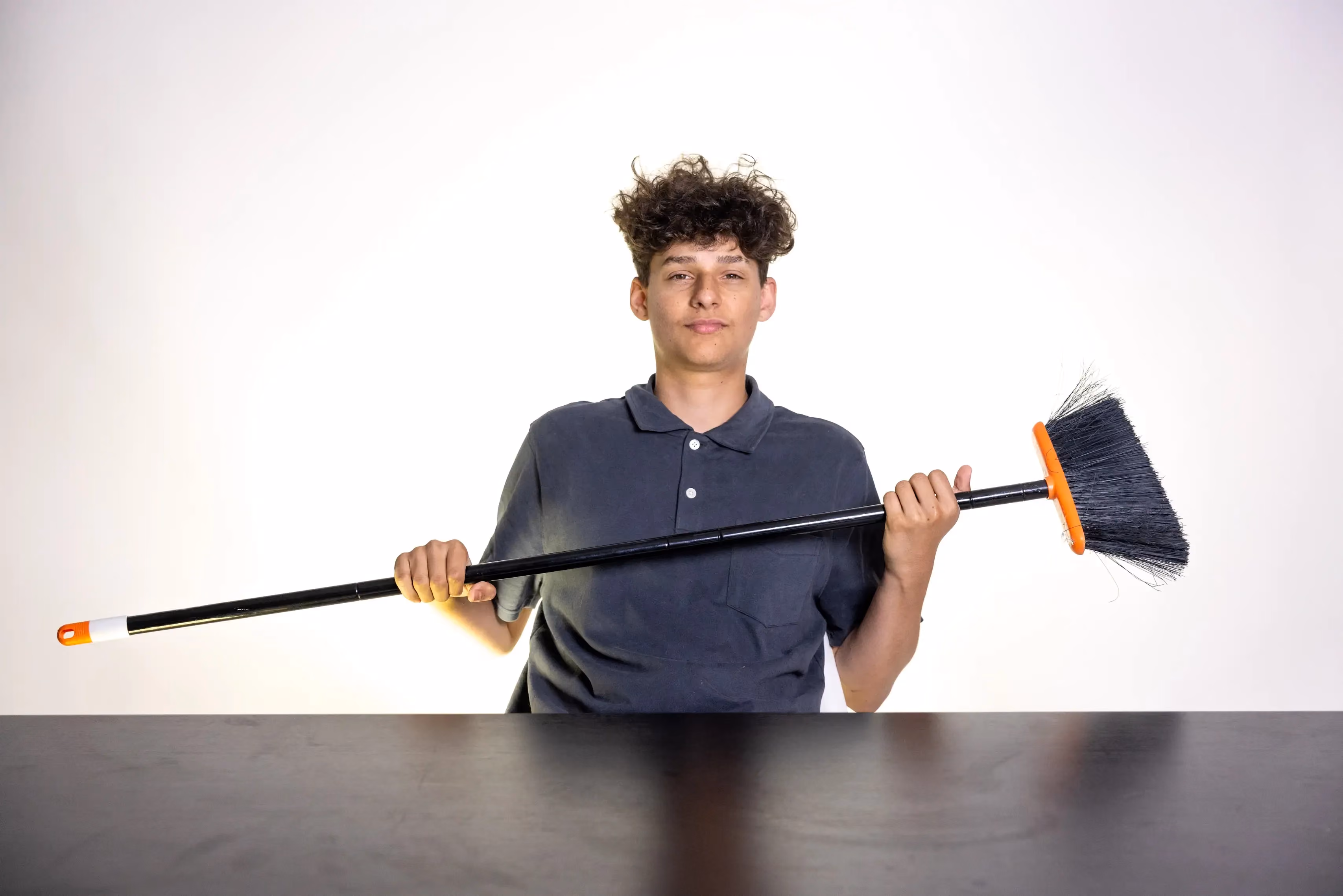 Kyle Carlsen holding a broom, reflecting his work in facilities support.