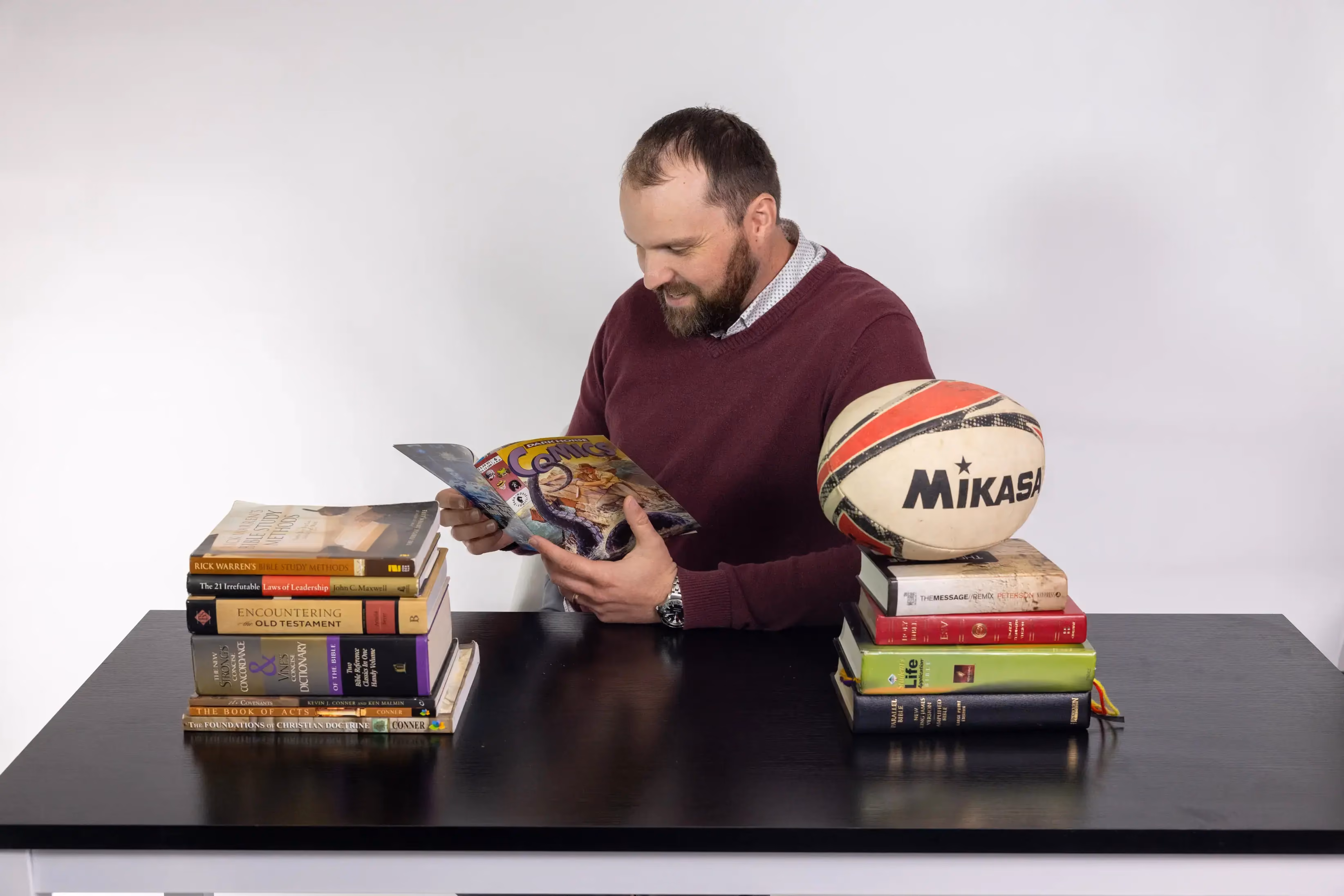 Jason Weir reading a book beside a rugby ball in a candid staff photo.