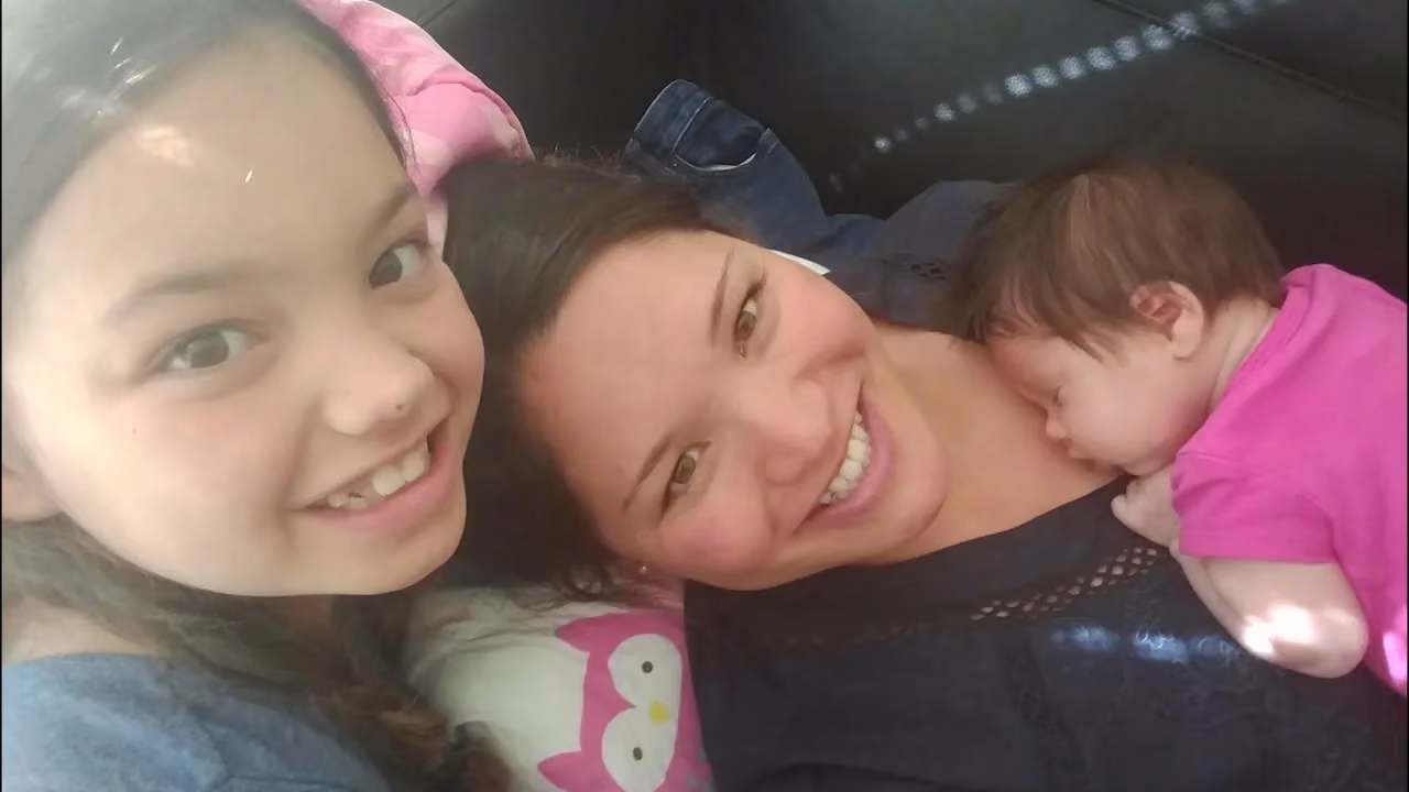 Woman smiling with two young girls in car seat.