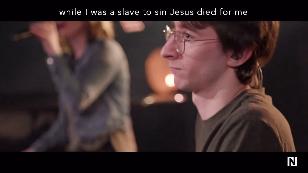 Man wearing glasses singing with text overlay above him.