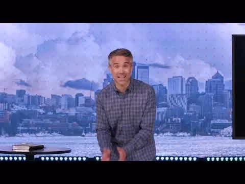 Man in plaid shirt smiling in studio with cityscape backdrop.