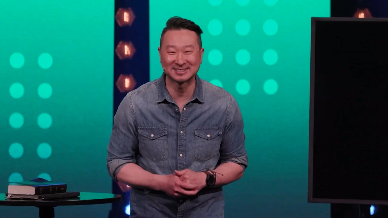 Man smiling in denim shirt against green lit backdrop with circular lights.