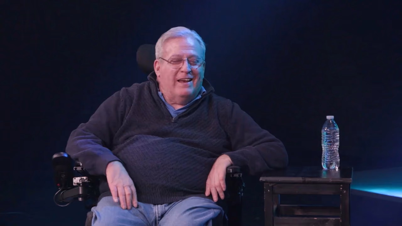 Man in wheelchair smiling with water bottle beside him.
