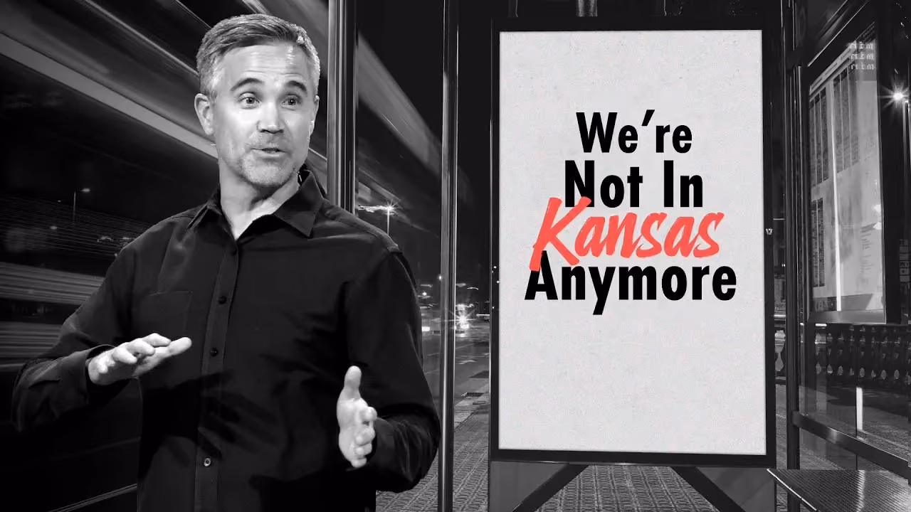 Man in black shirt standing beside a sign that reads We're Not In Kansas Anymore.