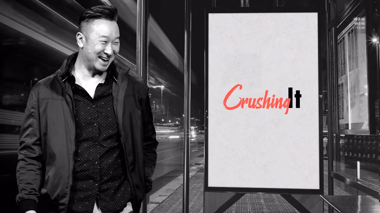 Man smiling beside a sign with 'Crushing It' logo in red and black. Nighttime urban setting.