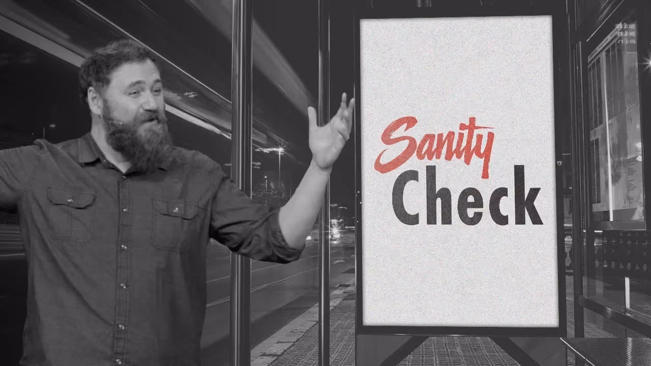 Man with beard pointing at a sign that reads Sanity Check.