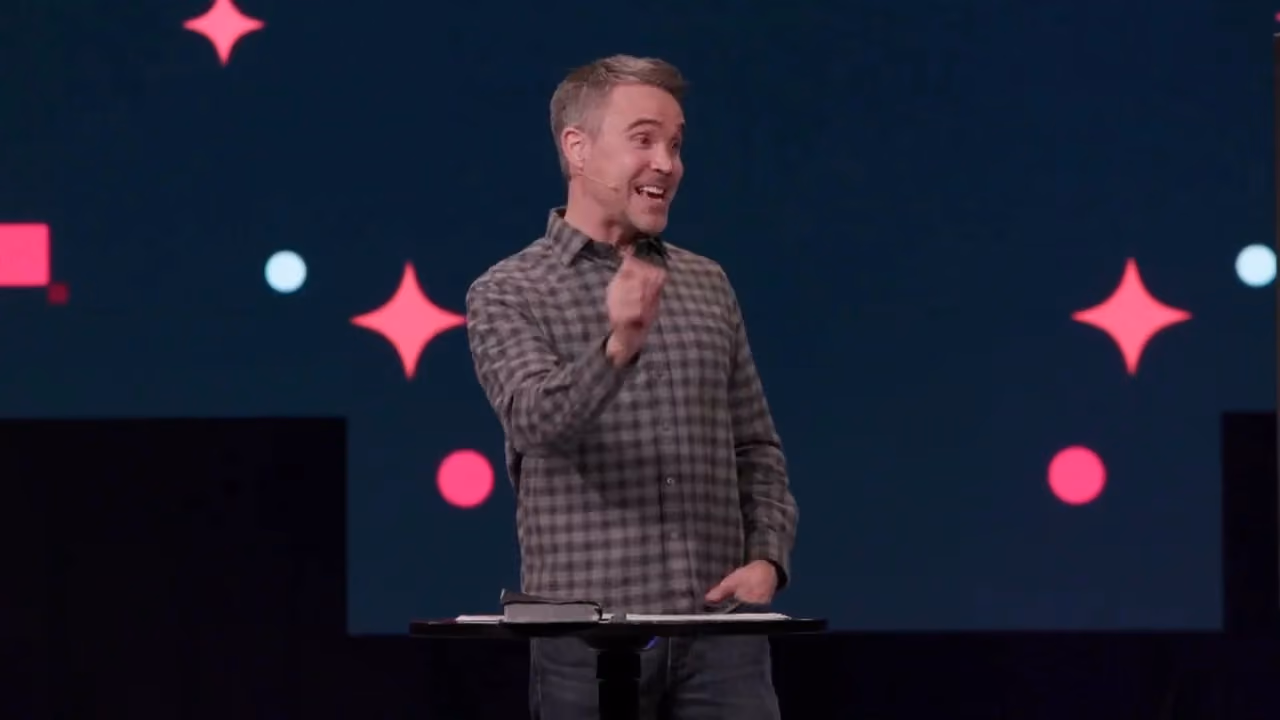 Man speaking at podium with colorful star and circle graphics behind him.