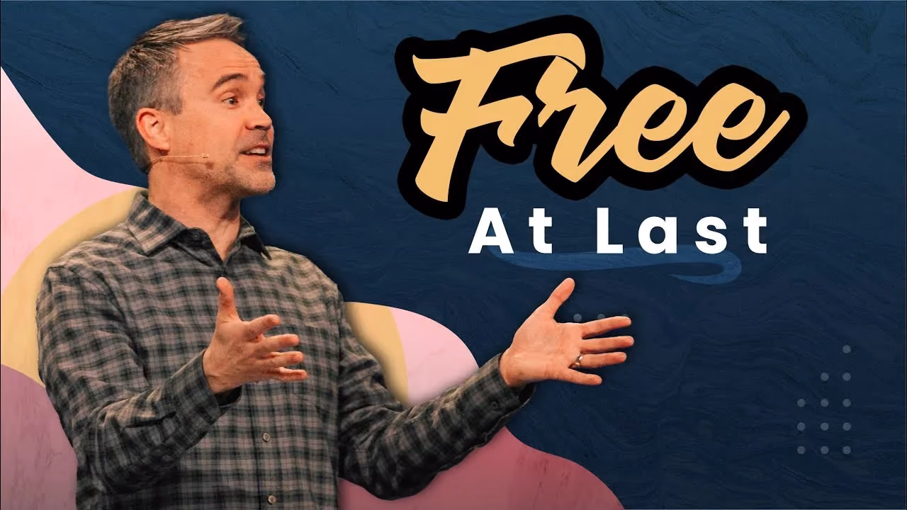 Free At Last, speaker in a plaid shirt gesturing with both hands open while preaching.