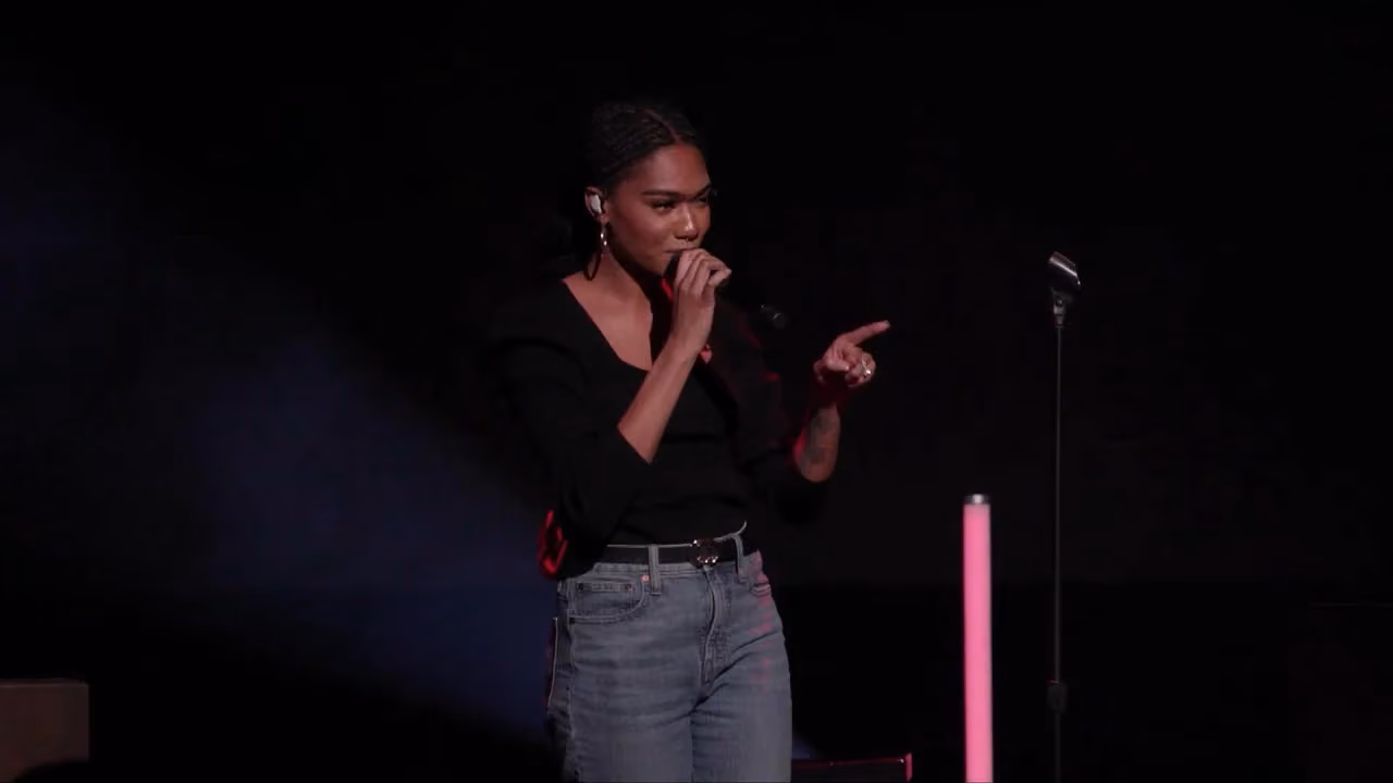 Good Friday service, a woman speaking into a handheld microphone on a dark, spotlit stage.