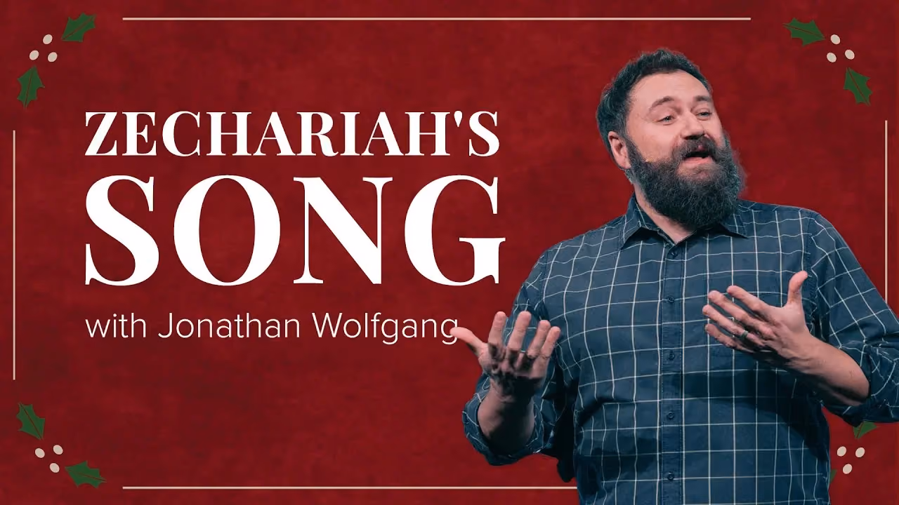 Zechariah's Song with Jonathan Wolfgang, hands open mid-sentence on a red holly backdrop.