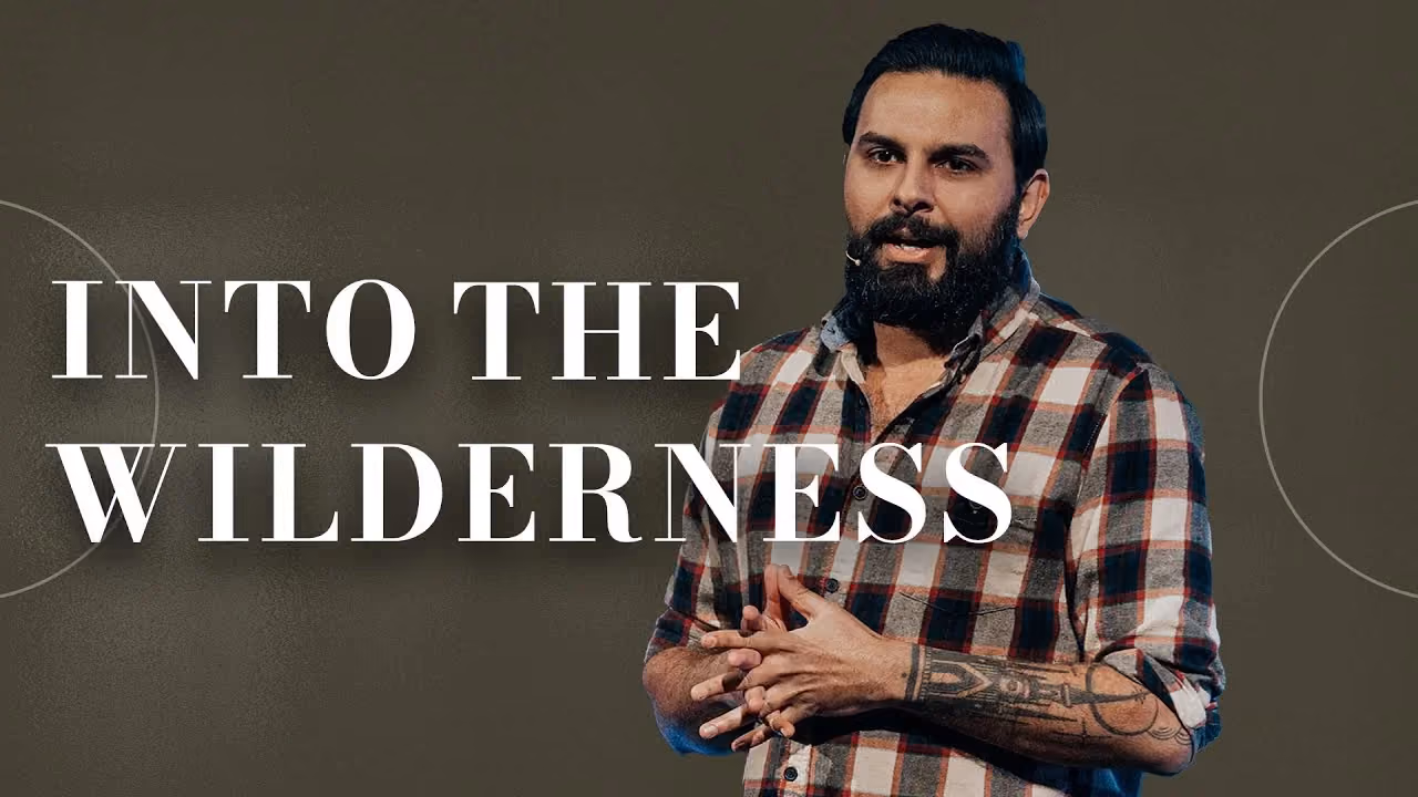 Into the Wilderness, speaker in a plaid shirt with hands clasped against an olive backdrop.