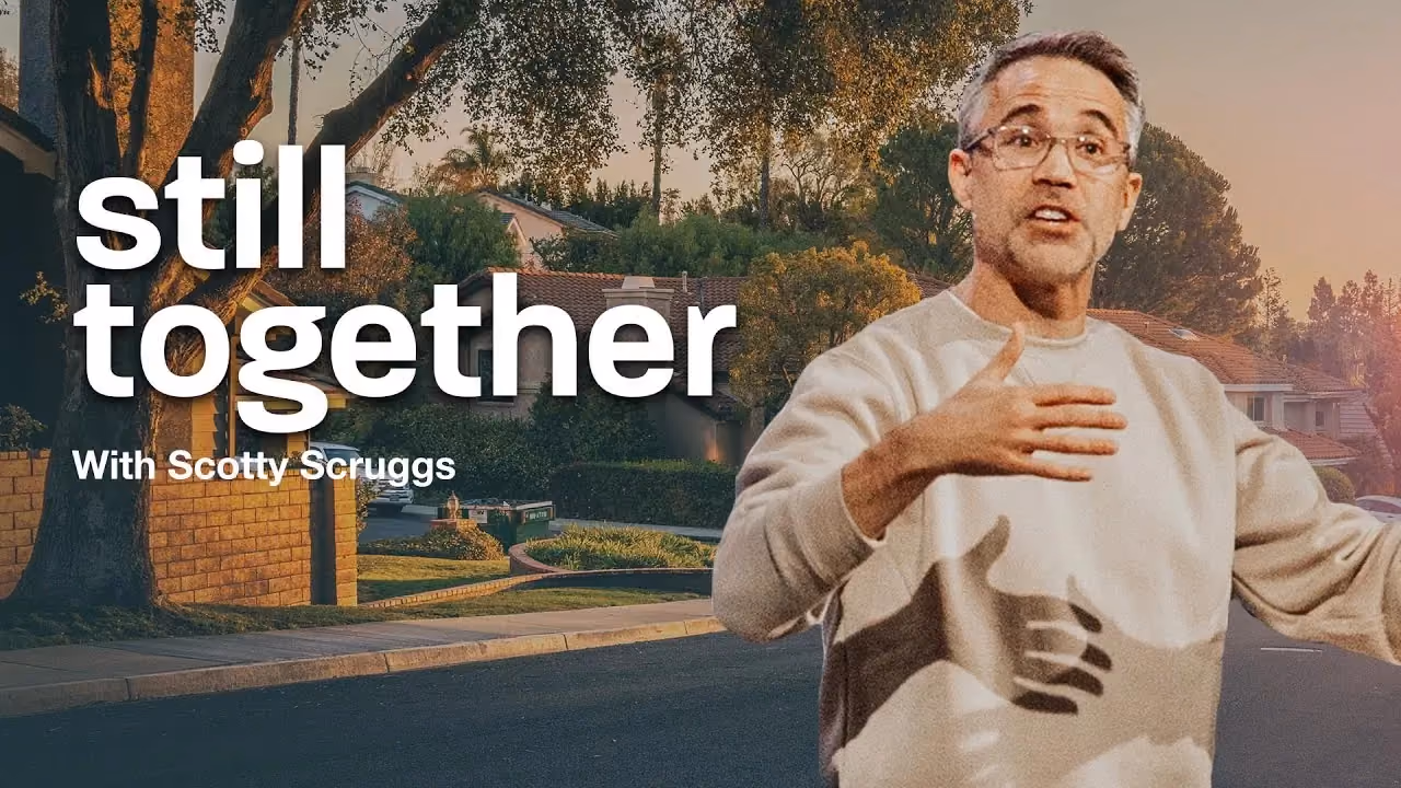 Still Together with Scotty Scruggs, hand on chest on a suburban street at sunset.