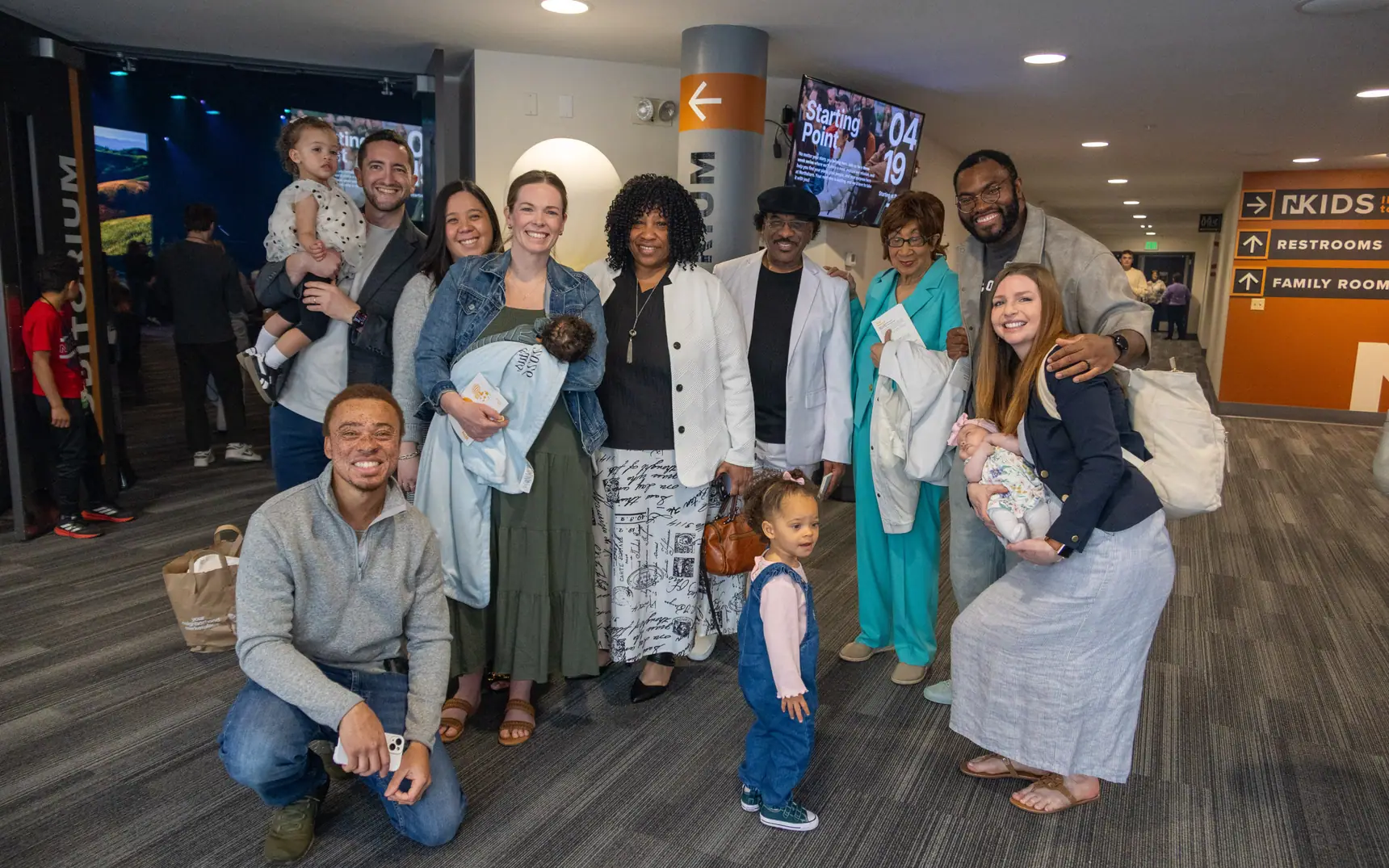 Photo of a large multigenerational group of church members gathered together in the lobby, several holding babies and young children