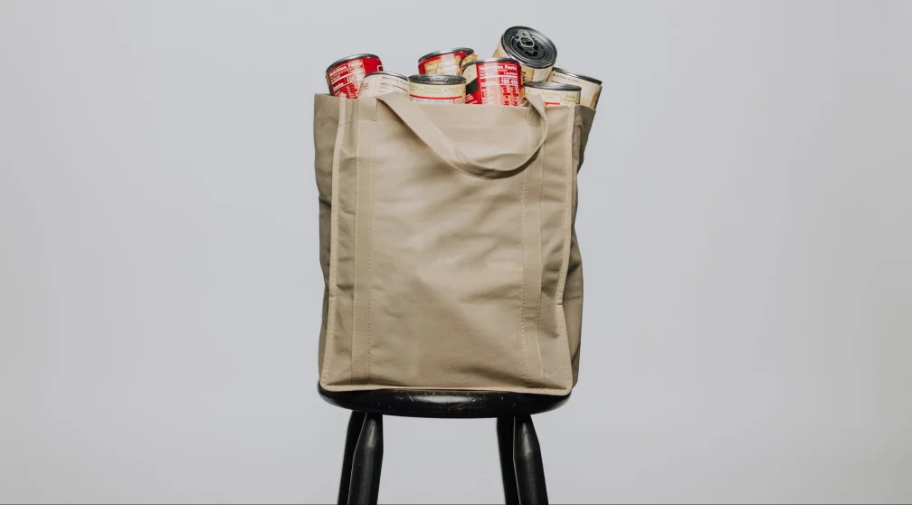 A beige tote bag filled with canned goods for a food drive.