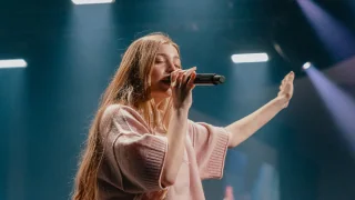 Photo of a woman singing into a microphone on stage during a worship service