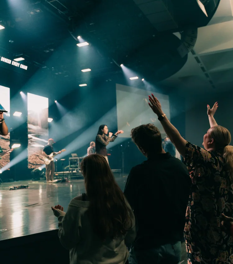 Photo of a worship band performing on stage as congregation members raise their hands during a service