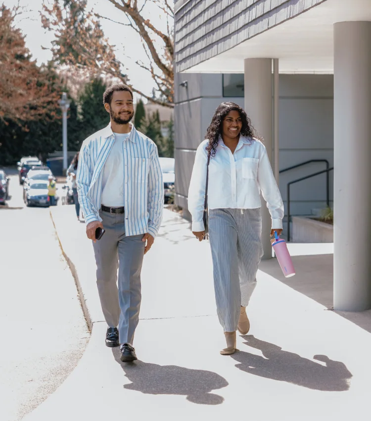 Photo of a man and woman smiling and walking together outside a building on a sunny day
