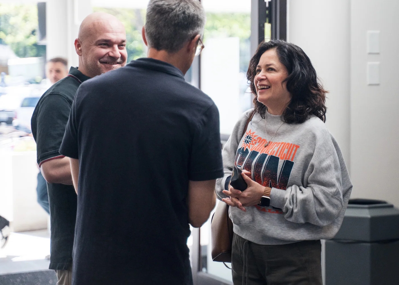 Photo of two men laughing together while talking with a woman inside a building lobby