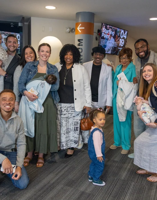Photo of a large multigenerational group of church members gathered together in the lobby, several holding babies and young children