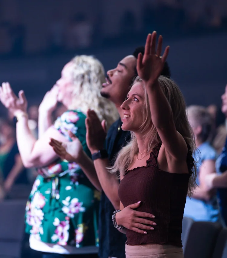 Photo of people with hands raised, clapping and worshiping during a service