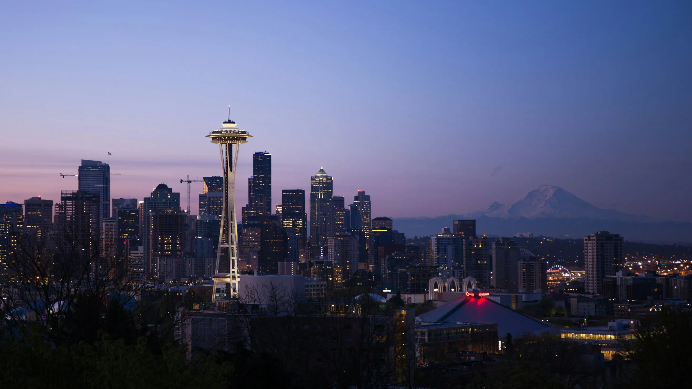 Seattle skyscrapers at dusk with mountains in the background.