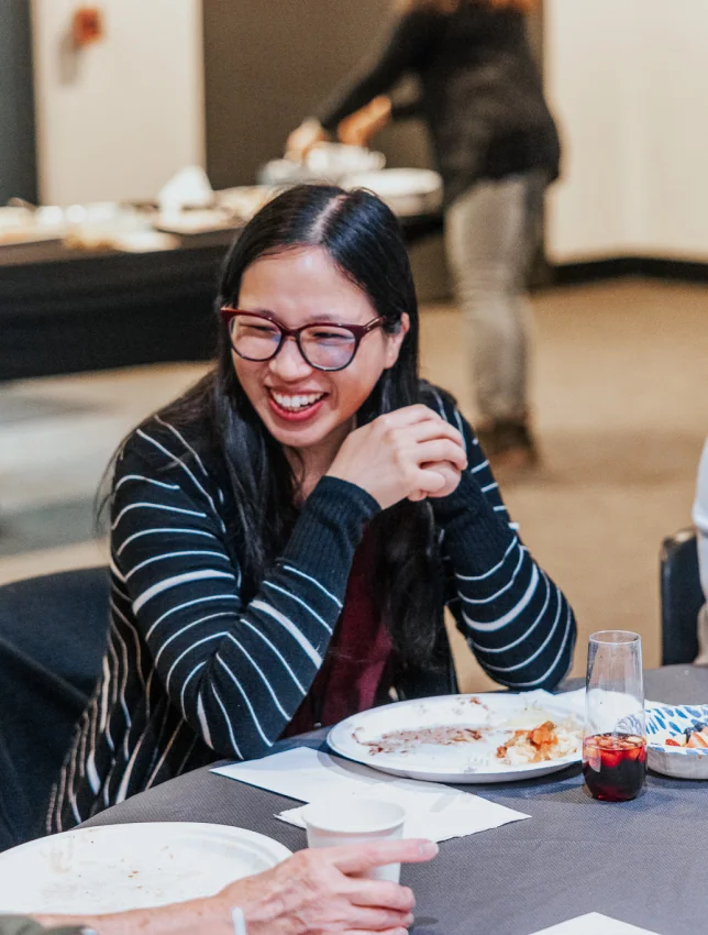 A woman laughing at a dinner table during a Connect gathering.