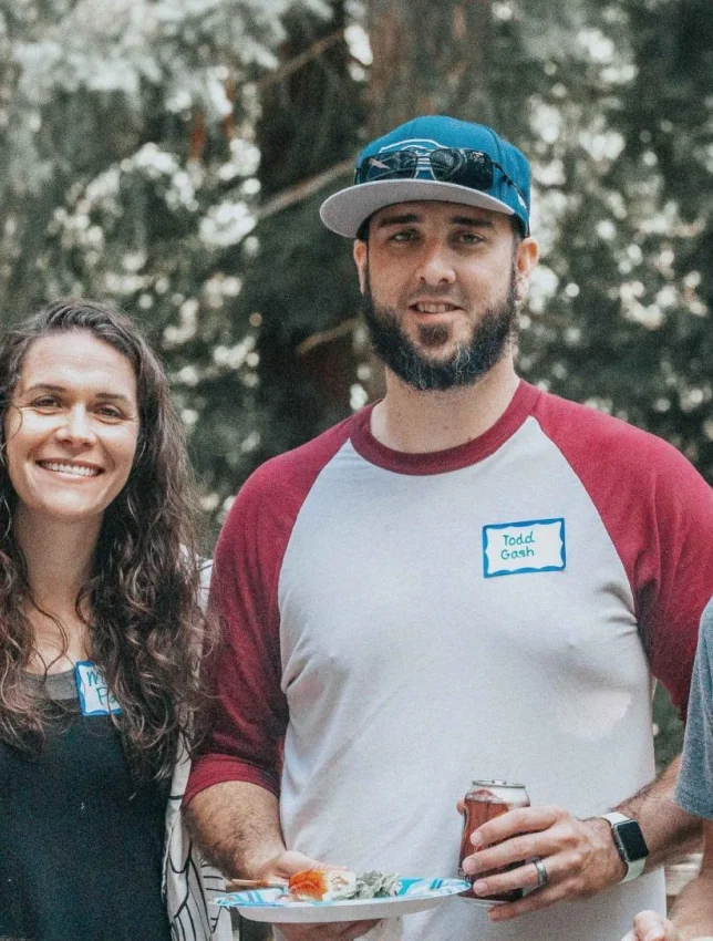 A man and woman holding food together outdoors at a gathering.