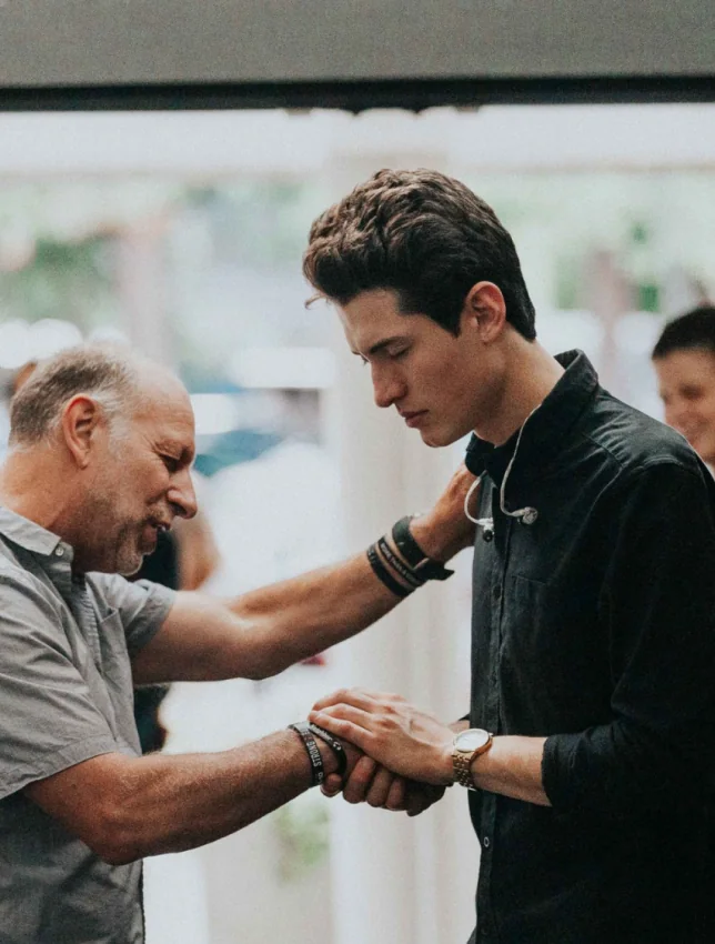 A man placing a hand on a young man's shoulder in fellowship.