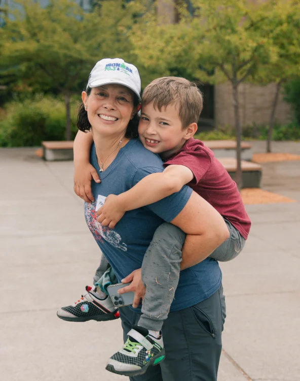 A mother carrying her son outdoors while volunteering.
