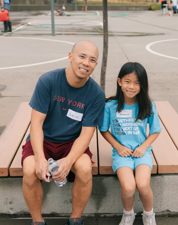 A man and a young girl smiling together on a bench.