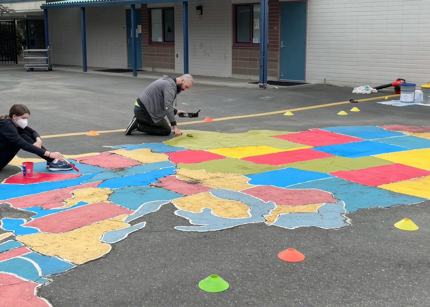 Volunteers painting a map of the United States on school pavement.