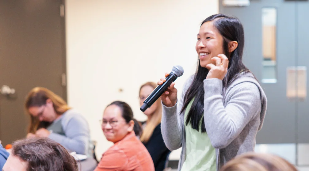 A woman speaking into a microphone at a MomCo event.