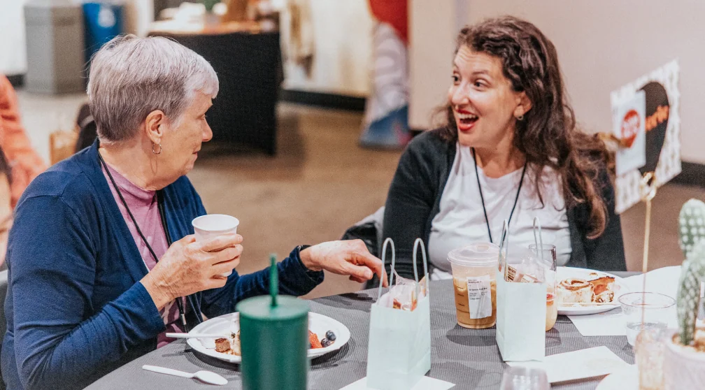 Two women laughing over a meal at a MomCo gathering.