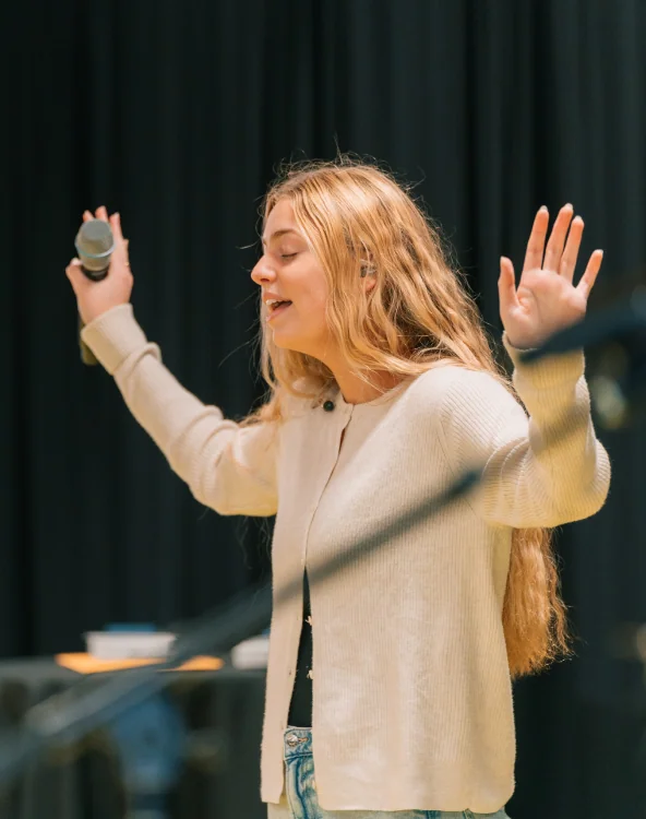 A woman singing into a microphone during worship.