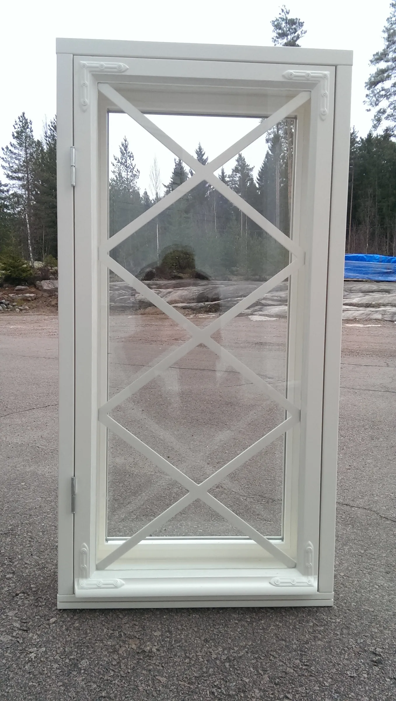 Valkoinen perinneikkuna ristikkoruuduilla ulkona asfalttikentällä.