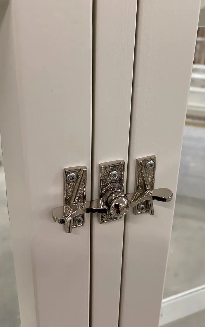 Valkoiseen puuoveen asennettu kiiltävä metallinen heloitus ja lukitusmekanismi.