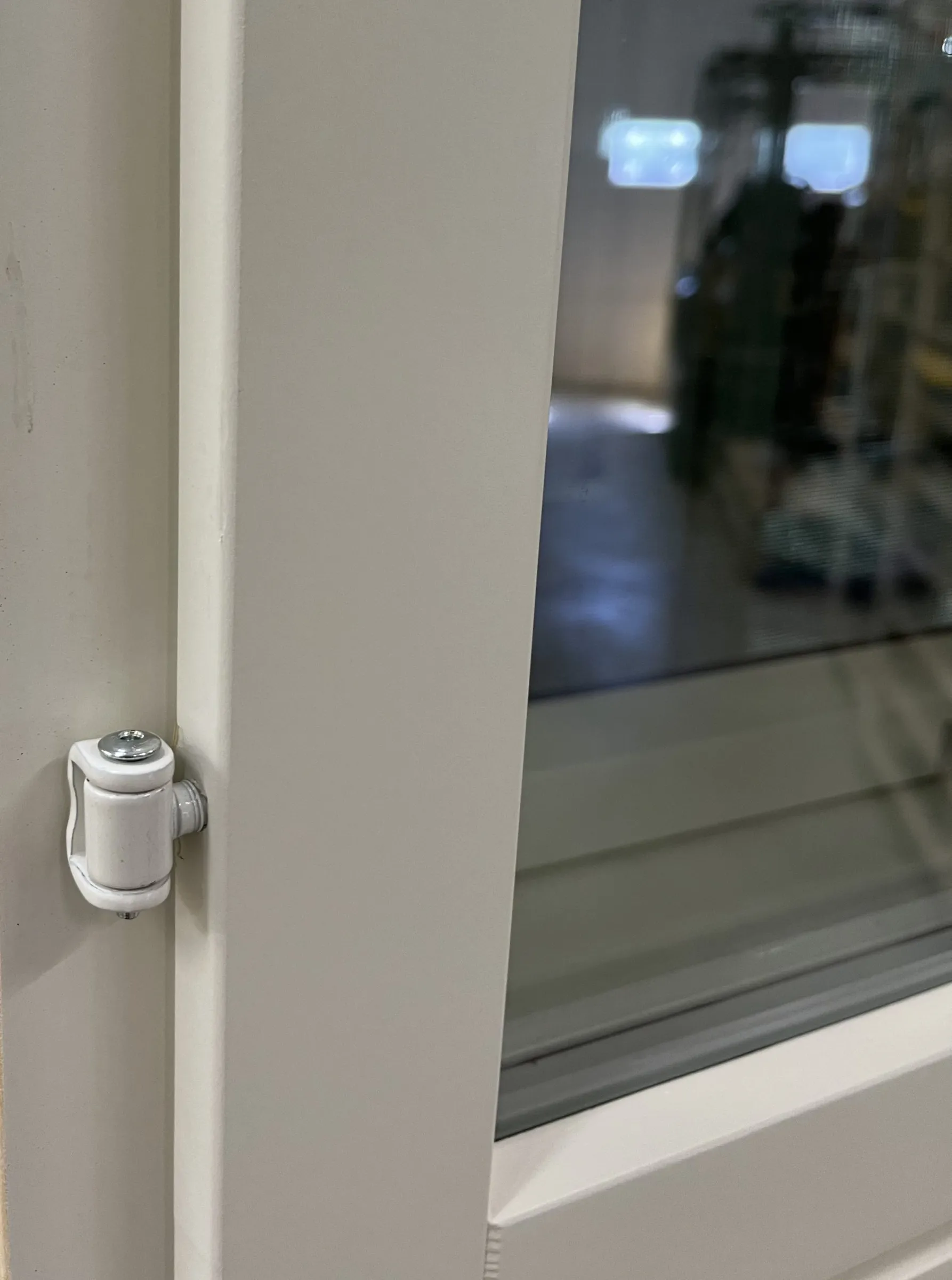 Valkoinen saranamekanismi kiinni vaaleassa puukas oy ulko-ovessa.