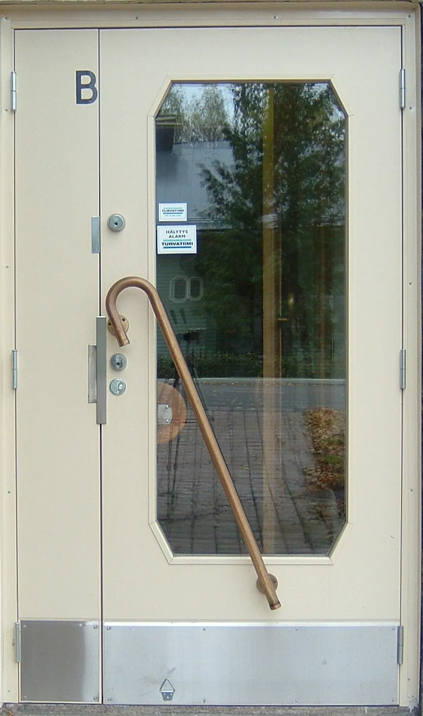 Vaalea ulkoovi, jossa on pitkä kaareva messinkinen vedin ja suuri ikkuna.