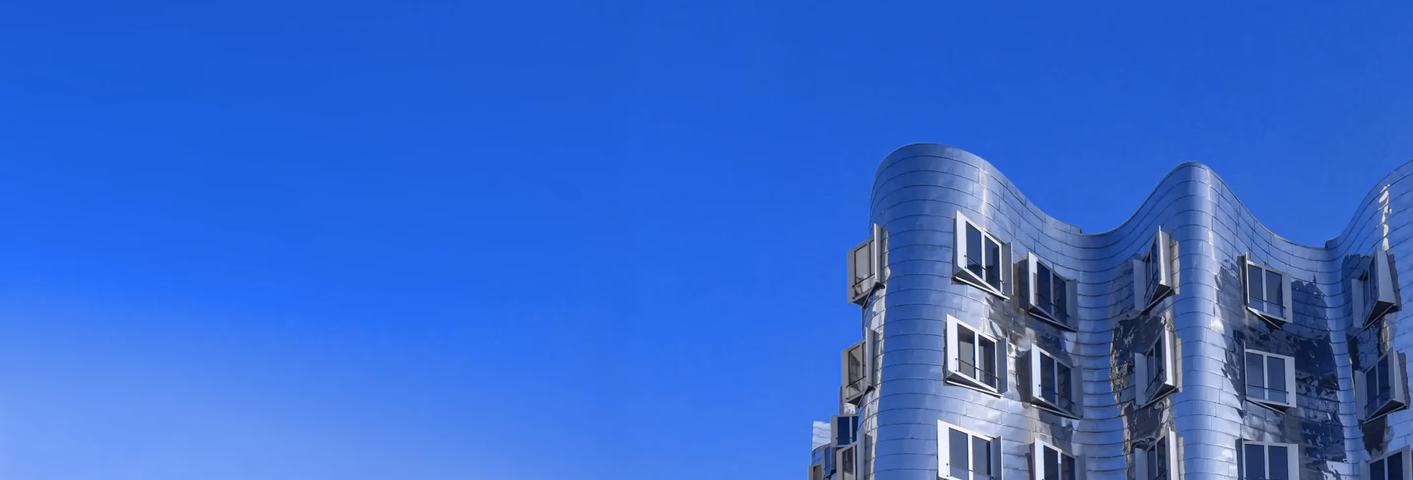 Modern wavy steel building with multiple windows under a clear blue sky. Next Inox