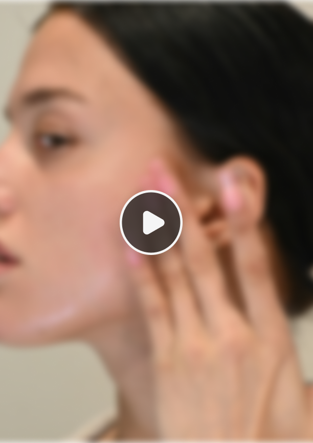 Blurred side profile of a woman touching her cheek with long nails.