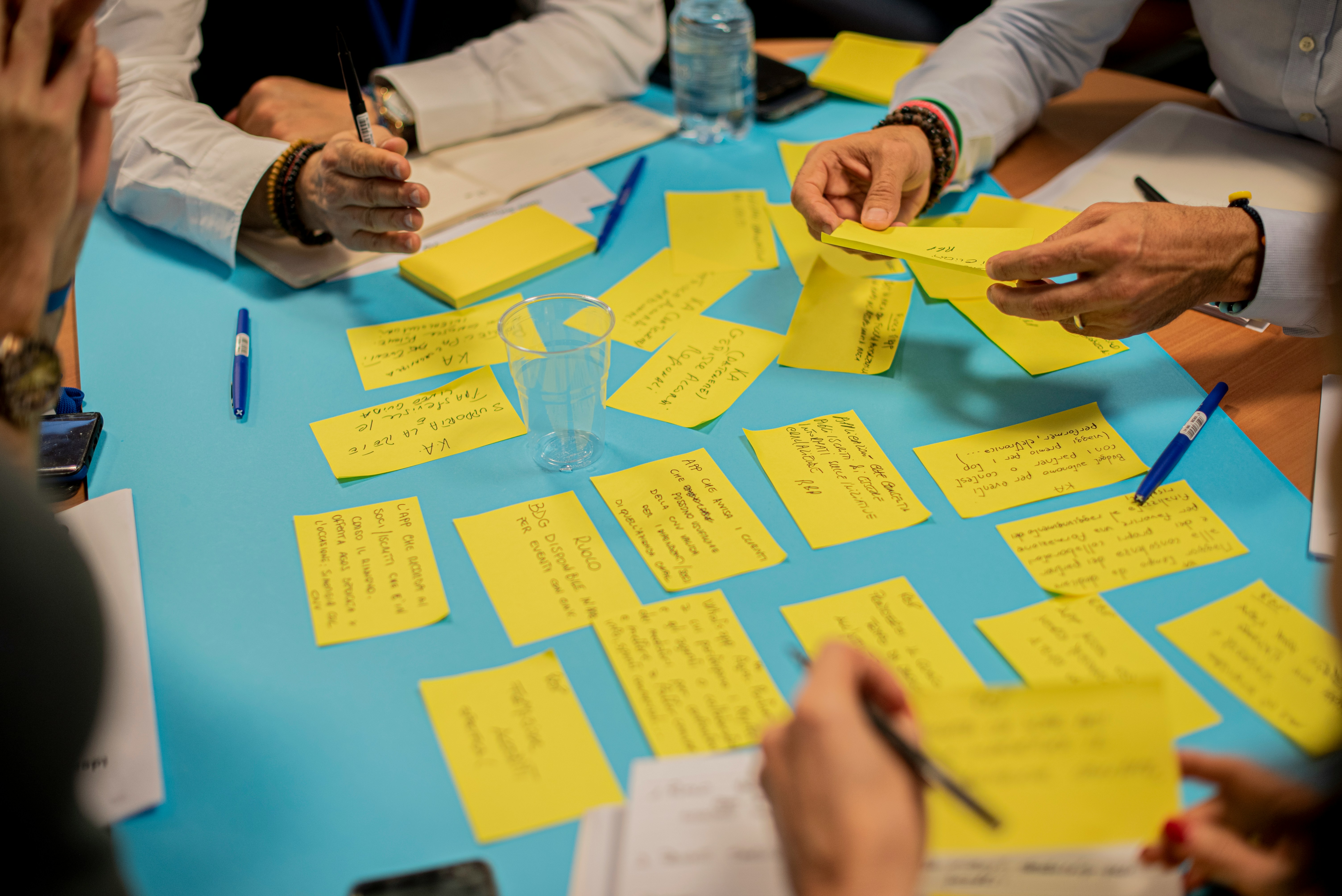 People collaborating at a table with yellow sticky notes, pens, and a clear plastic cup.