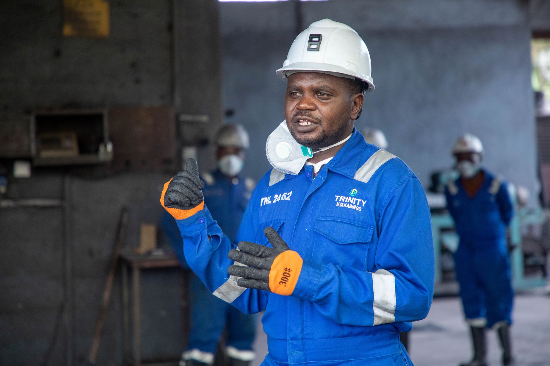 A frontline worker in a hard hat and safety gear leading a briefing on the factory floor