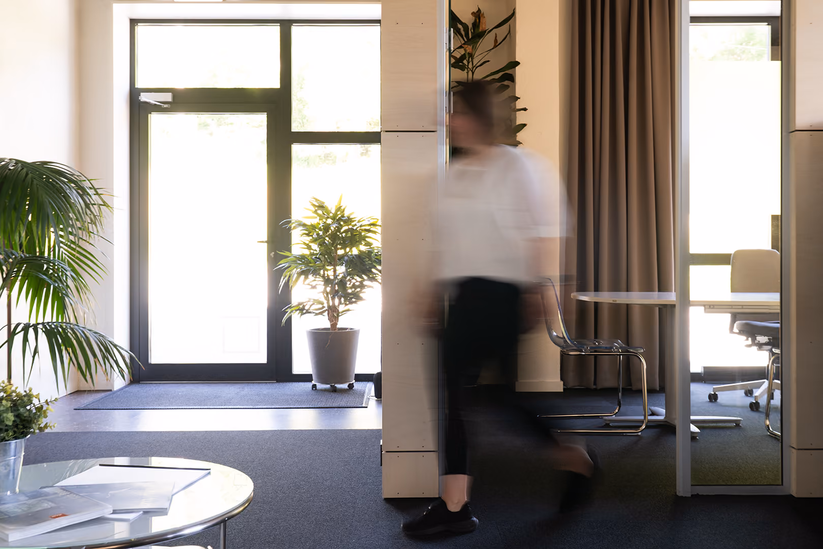 Medarbeider går gjennom kontorlokalet med planter og et møterom i bakgrunnen