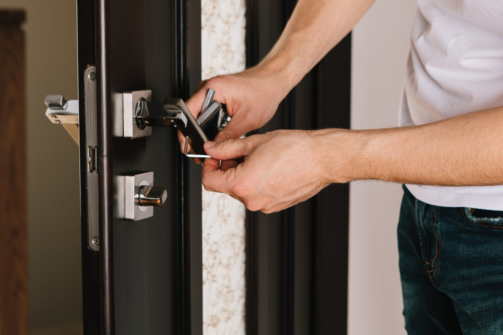 Locksmith using a set of lock picks on a wooden door, with two people watching in background.