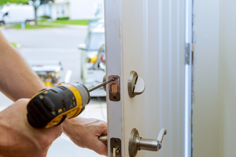 Locksmith using a cordless drill to install a deadbolt on a white front door, with a mobile service van parked at the curb in Venice FL