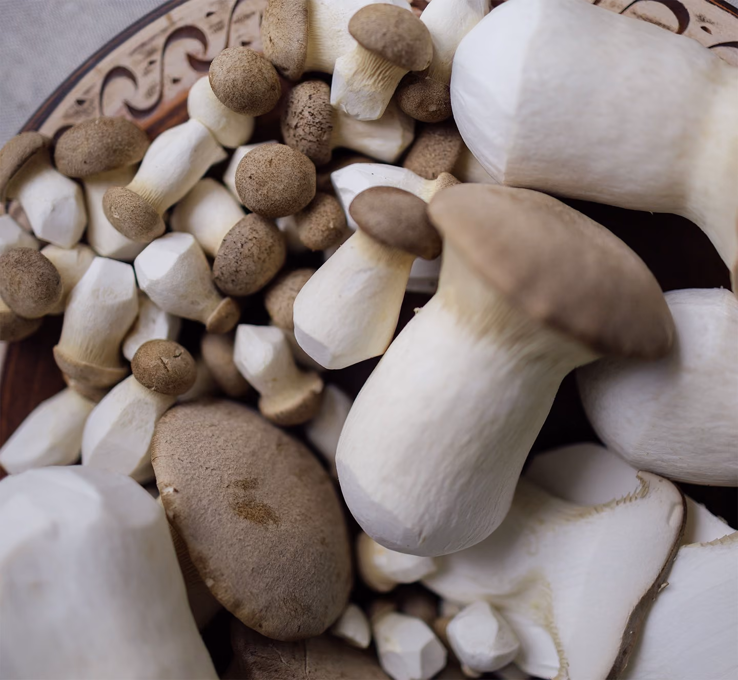 Close-up of several fresh king oyster mushrooms with thick stems and brownish caps on a wooden plate.