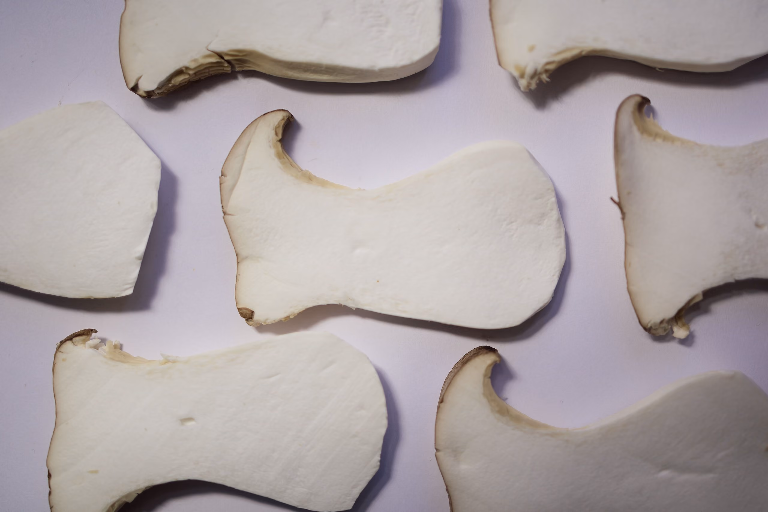 Close-up of sliced white mushrooms with dark edges on a light surface.