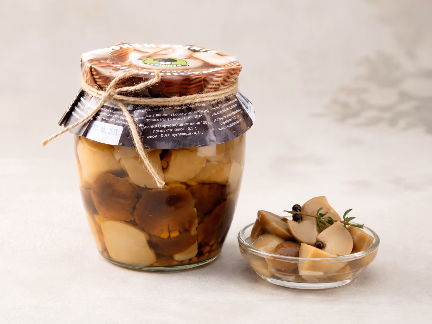 Glass jar of marinated mushrooms next to a small bowl of sliced marinated mushrooms with herbs.