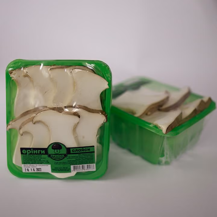 Two green plastic trays of sliced king oyster mushrooms sealed in clear plastic wrap.