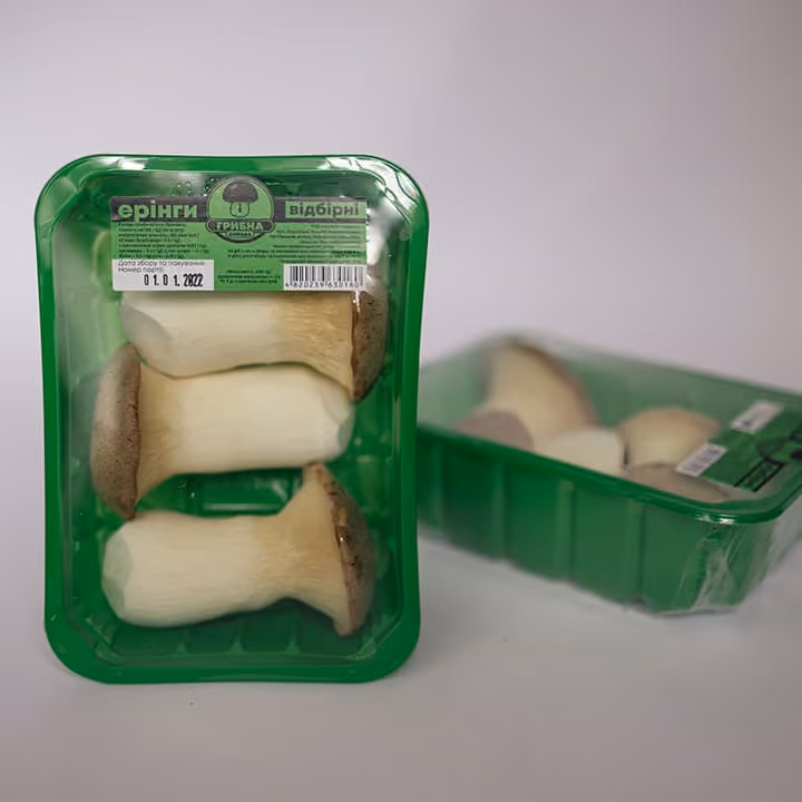 Three king oyster mushrooms in green plastic packaging with a second package blurred in the background.